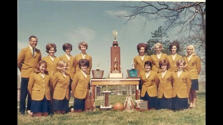 Formal photograph of Porter High School State Champion Girls Basketball team in gold blazers and their coach Galen Johnson and the State Trophy; Porter High School building in the background.